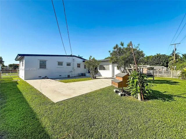 Single-story residence featuring a smooth stucco exterior, concrete patio, expansive lawn, and perimeter fencing