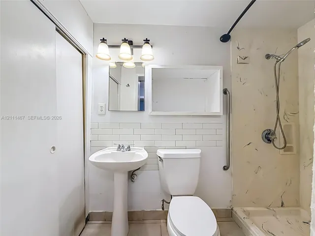 Bathroom featuring a pedestal sink, white subway tile backsplash, wall-mounted three-light fixture, mirror with integrated cabinet, and a walk-in shower with a handheld showerhead