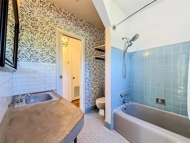 Bathroom featuring a concrete countertop with a recessed sink, white subway tile backsplash, blue ceramic tile shower surround, and patterned wall covering