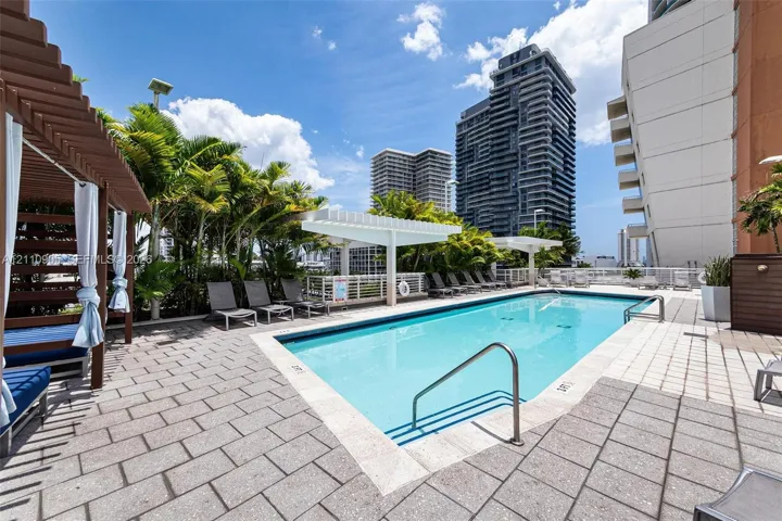 Swimming pool with stone paver decking, wood-frame cabana, and white pergola structures