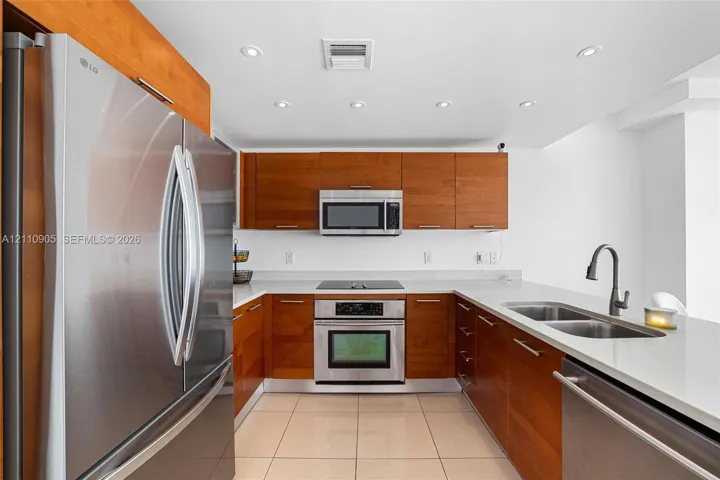 Kitchen featuring wood-finish cabinetry, solid surface countertops, stainless steel appliances, recessed ceiling lighting, and large-format tile flooring