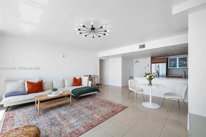Open-concept interior featuring oversized light-toned floor tiling, a matte black multi-arm sputnik chandelier, and kitchen cabinetry with integrated stainless steel appliances