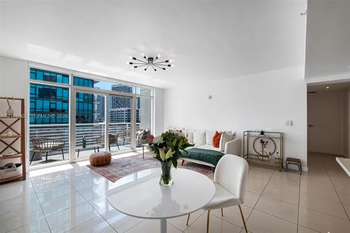 Open-concept interior featuring large-format tile flooring, floor-to-ceiling glass sliding doors, a private balcony with horizontal metal railing, and a contemporary multi-arm sputnik ceiling light fixture