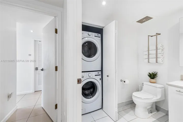 Stacked front-loading washer and dryer, one-piece dual-flush toilet, and light-toned tile flooring