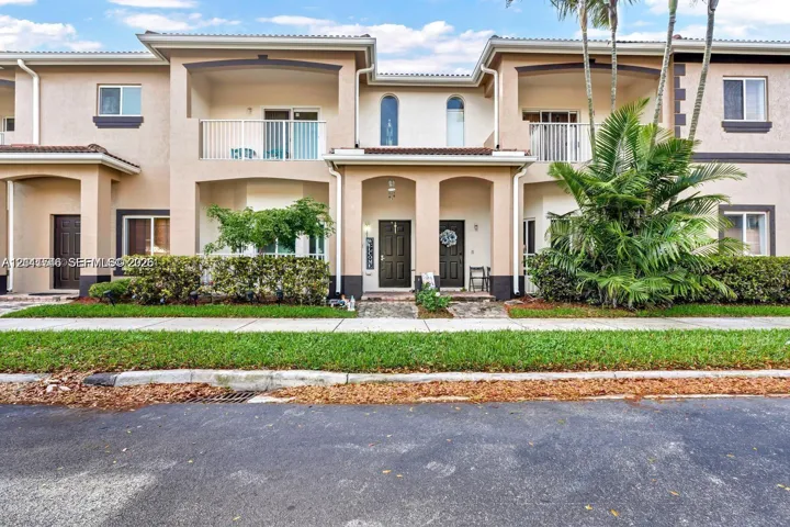 Two-story stucco exterior featuring arched architectural detailing, dual second-story covered balconies with white metal railings, and stone-paved entryway paths