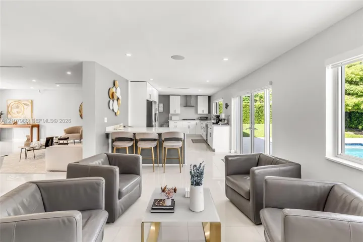 Open-concept kitchen featuring white cabinetry, quartz countertops, a breakfast bar, recessed lighting, and large-format tile flooring