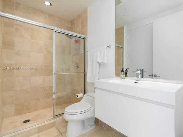 Modern wall-mounted vanity with a rectangular sink, stone-tiled walk-in shower with a glass enclosure, and large-format wall mirror