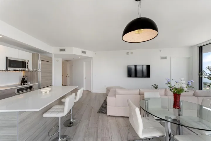 Open-concept kitchen featuring an expansive island with a quartz countertop, integrated cabinetry, stainless steel appliances, and wood-finish flooring with a dome pendant light fixture