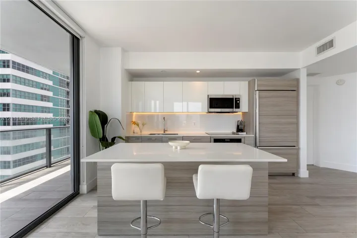 Kitchen featuring a white quartz island, high-gloss flat-panel cabinetry, integrated refrigerator, wood-finish lower cabinetry, and floor-to-ceiling glass sliding doors