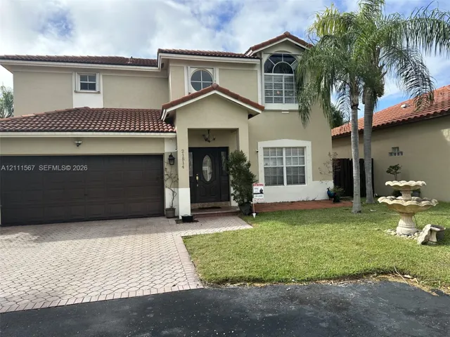 Two-story exterior featuring a stucco facade, tile roof, arched window detailing, paver driveway, and a front garden fountain