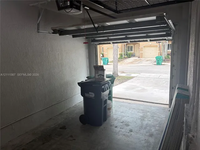 Enclosed garage featuring a concrete floor, textured walls, and an overhead automatic door opener