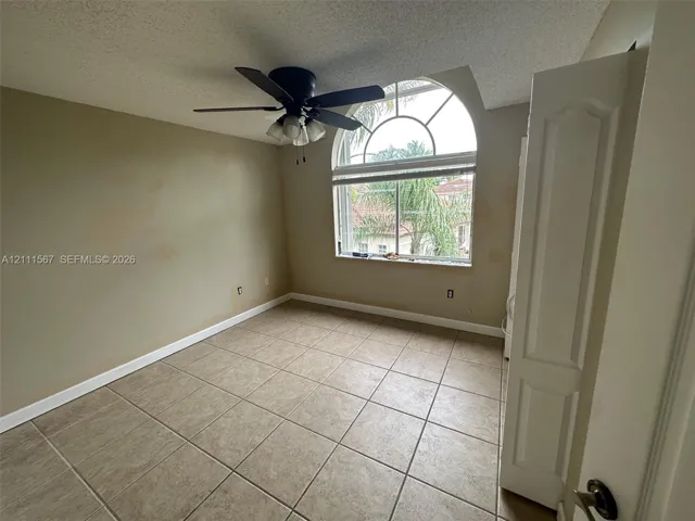 Arched window with decorative muntins, ceramic tile flooring, and integrated ceiling fan with multi-light fixture