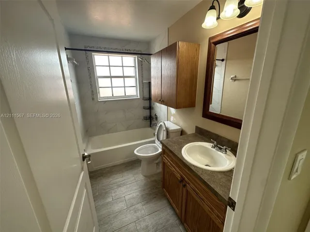 Bathroom featuring a vanity with dark-tone countertop, wood-finish cabinetry, tile-surround tub, and tile flooring