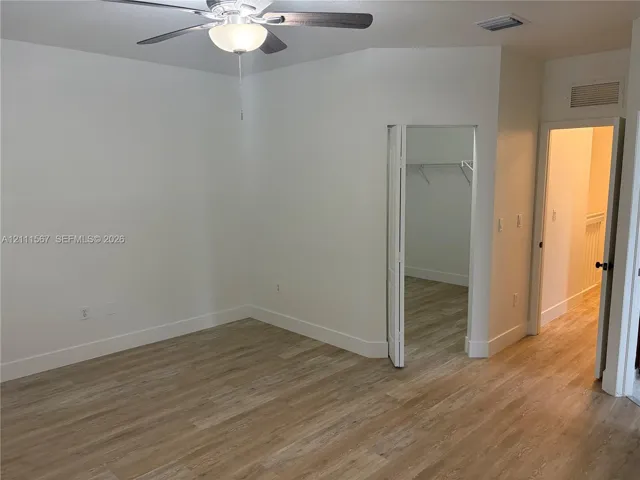 Wood-finish flooring, vaulted ceiling, and ceiling fan with integrated lighting, featuring a walk-in closet with wire shelving
