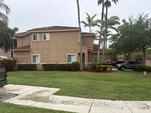 Two-story exterior featuring a stucco facade, clay tile roof, and mature palm trees with manicured landscaping