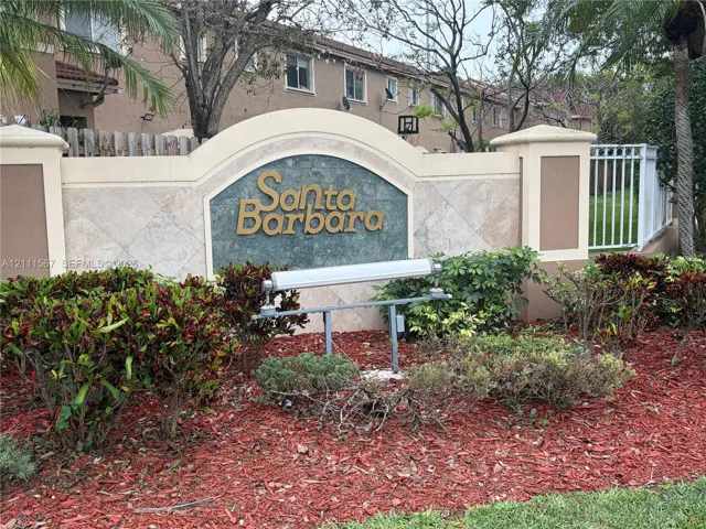 Stucco monument signage featuring stone-tile accents, metal lettering, and integrated landscape lighting, set within a manicured garden bed