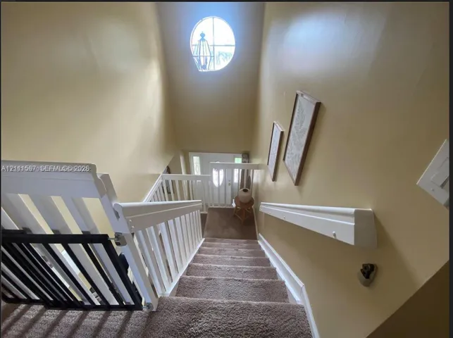 Staircase featuring white balusters, a wooden handrail, carpeted steps, and a circular accent window