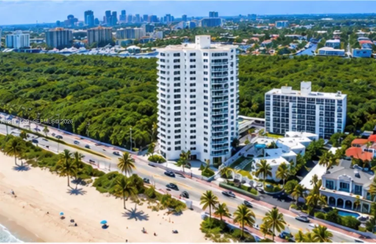 High-rise residential tower featuring a white facade, private balconies, an attached swimming pool, landscaped grounds, and immediate proximity to the coastline