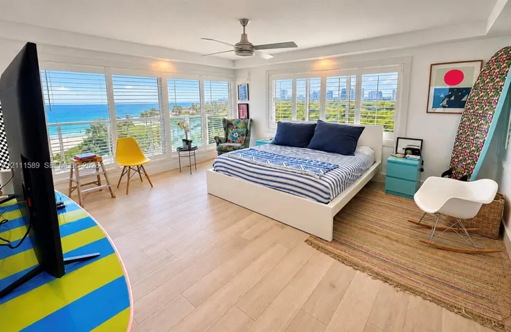 Extensive window walls with coastal scenery, wood-finish flooring, ceiling fan, and adjustable shutter window coverings