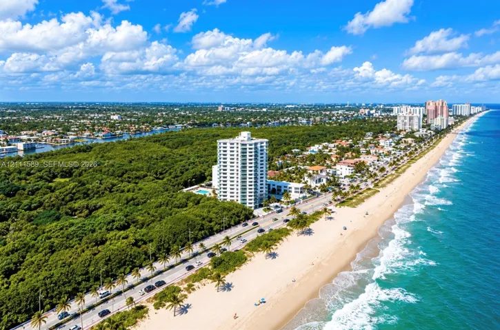 Aerial perspective of coastal high-rise property featuring direct proximity to the shoreline, surrounding mature vegetation, and expansive ocean frontage