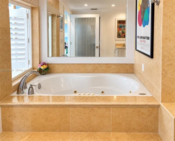 Jetted soaking tub with deck-mounted faucet, framed by stone-tile surround and a wall-to-wall mirror with white trim