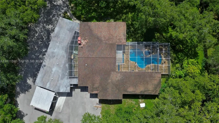 Aerial perspective featuring a multi-level roofline, screened-in swimming pool enclosure, detached covered parking structure, and mature trees on a wooded lot