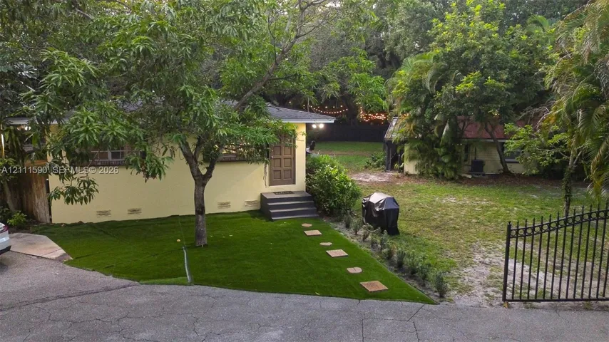 Stucco exterior dwelling featuring a multi-panel wood door, concrete paver pathway, artificial turf lawn, and ornamental metal fencing