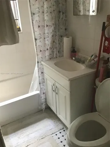 Bathroom featuring a white vanity cabinet with a stone-top integrated sink, a built-in shower and tub combination, white wall tiling, and black-and-white mosaic tile flooring