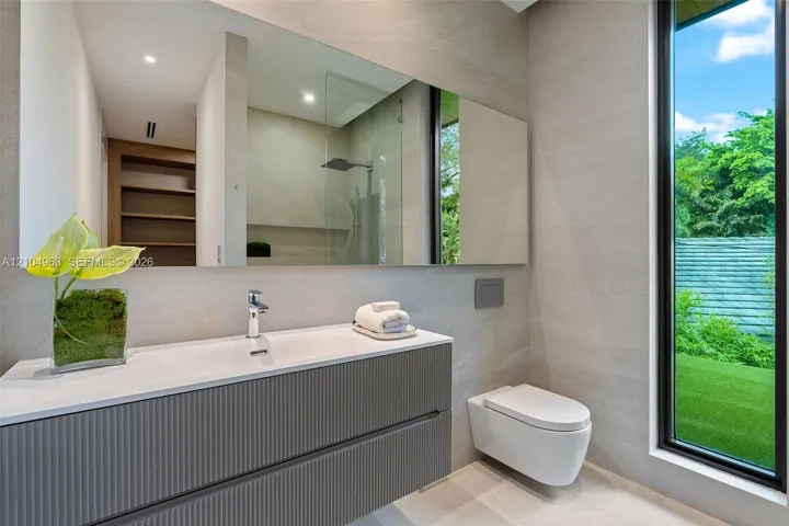 Floating gray vanity with a textured front, white countertop, wall-mounted toilet, full-width mirror, and floor-to-ceiling window