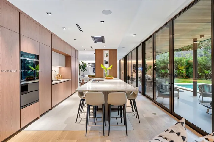 Kitchen featuring floor-to-ceiling wood-finish cabinetry, central island with stone countertop, recessed lighting, and full-length glass sliding doors leading to the exterior patio and pool area