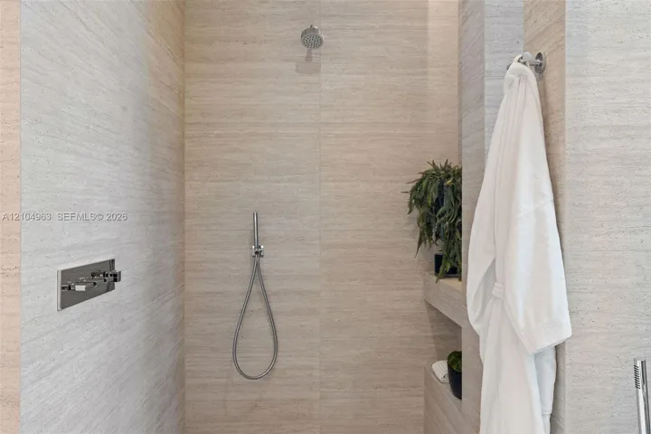 Walk-in shower featuring large-format textured stone wall tile, built-in shelving, a rainfall showerhead, and a wall-mounted handheld shower fixture with chrome hardware