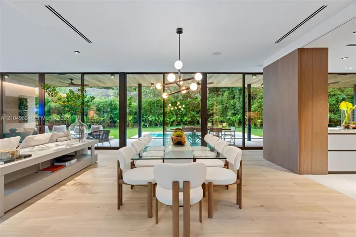 Floor-to-ceiling glass walls, wood-finish flooring, linear recessed lighting, integrated wall cabinetry, and a contemporary multi-arm chandelier
