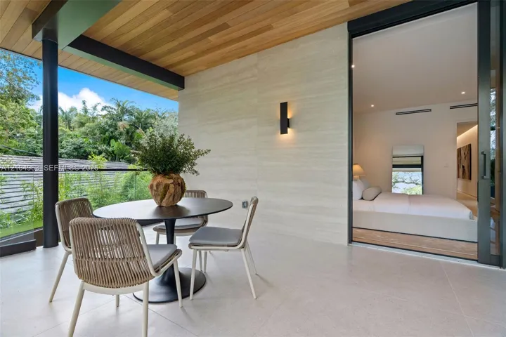 Covered balcony featuring wood-paneled ceiling, stone-finish wall cladding, large-format tile flooring, frameless glass railings, and expansive sliding glass doors