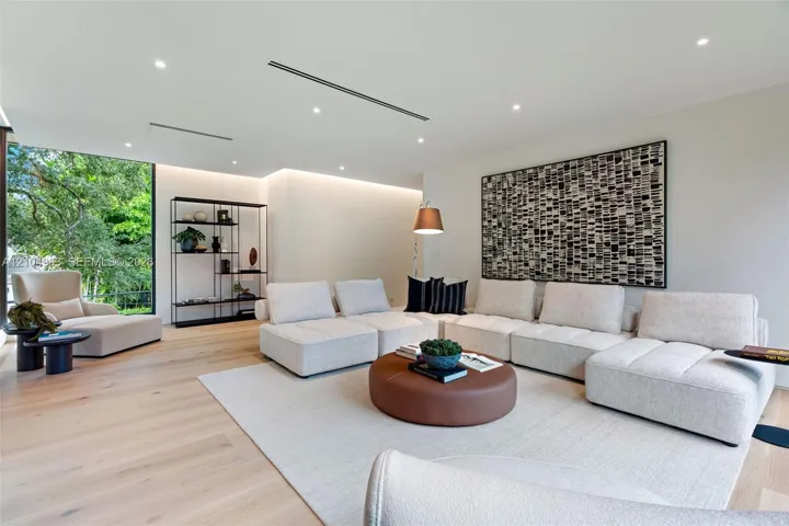 Living area featuring light wood-finish flooring, recessed linear lighting, hidden cove accent lighting, and a large floor-to-ceiling glass panel
