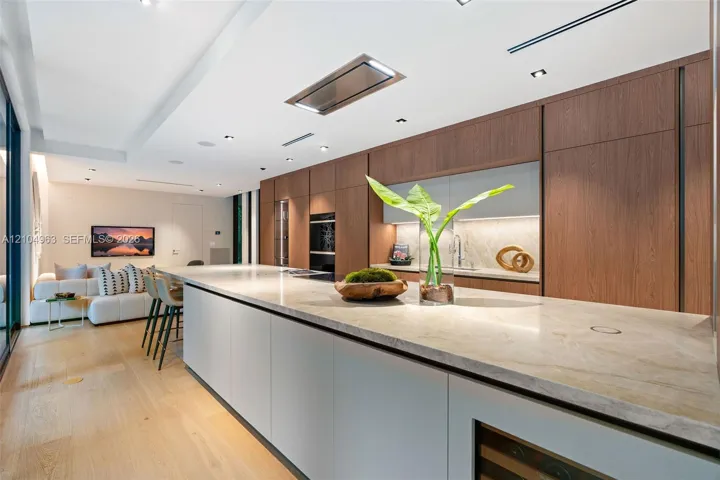 Kitchen featuring full-height wood-finish cabinetry, a lengthy stone-surfaced island, integrated double wall ovens, a built-in wine refrigerator, and light wood-finish flooring