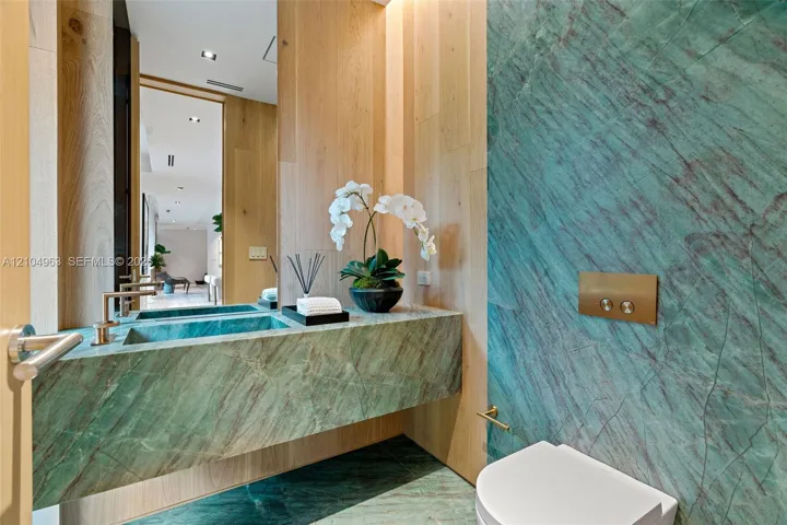 Floating vanity with integrated basin, teal stone wall cladding, floor-to-ceiling wood paneling, wall-mounted metallic flush actuator, and recessed ceiling lighting