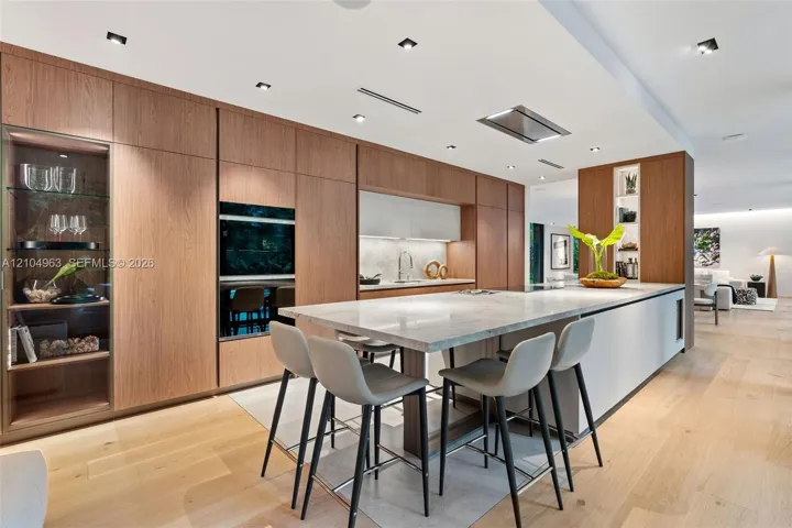 Kitchen featuring flat-panel wood cabinetry, integrated stainless steel double wall ovens, a stone-topped island with waterfall edge, and wood-finish flooring