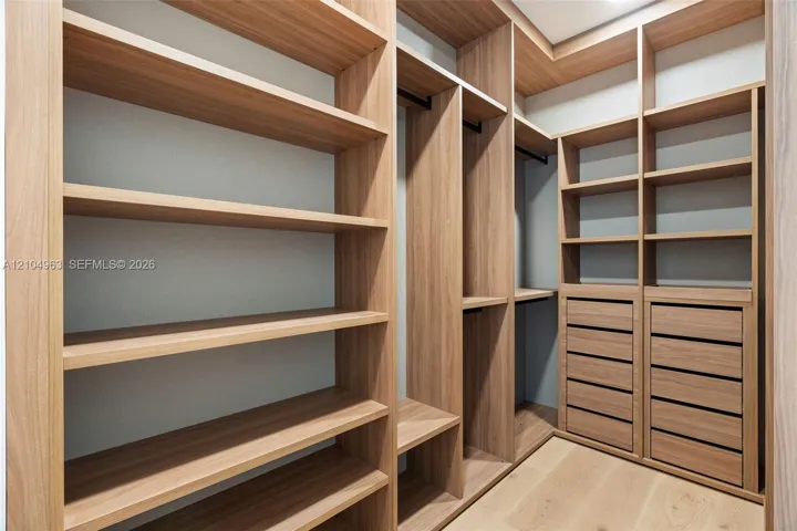 Custom walk-in closet featuring built-in wood-finish shelving, integrated hanging rods, and multi-drawer cabinetry with wood-finish flooring