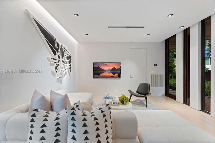 Contemporary interior featuring smooth wall panels, light-toned wood-finish flooring, recessed ceiling lighting, and floor-to-ceiling windows with dark frames