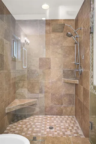 Walk-in shower featuring floor-to-ceiling stone-finish tile, a glass enclosure, dual shower heads, a built-in corner bench, and a mosaic-tile floor