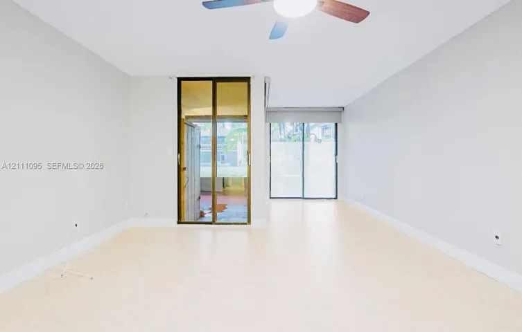 Neutral-toned interior featuring large-format tile flooring, dual sliding glass doors, and a ceiling fan with integrated lighting
