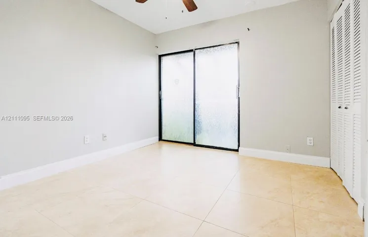 Interior space featuring oversized neutral tile flooring, sliding glass doors, white louvered-style closet doors, and a ceiling fan