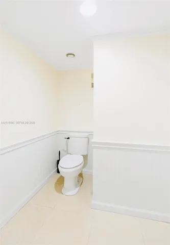 White beadboard wainscoting with chair rail molding, neutral tile flooring, and a porcelain toilet