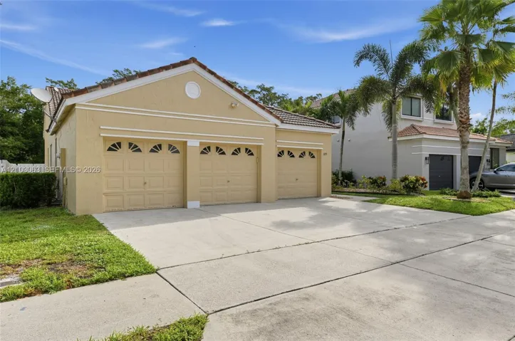 Stucco exterior featuring a three-car garage with arched window detailing, tile roofing, and a concrete driveway