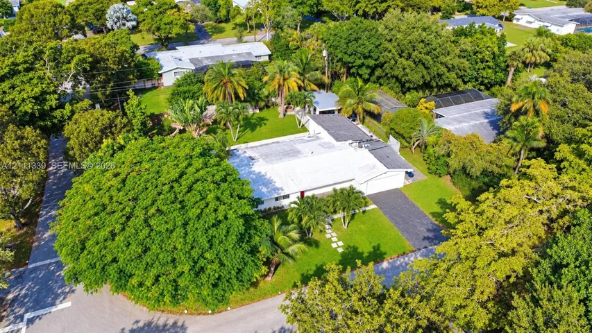 Aerial perspective of a low-profile residence featuring a light-colored roof, attached garage, paved driveway, stone paver walkway, and mature landscaping