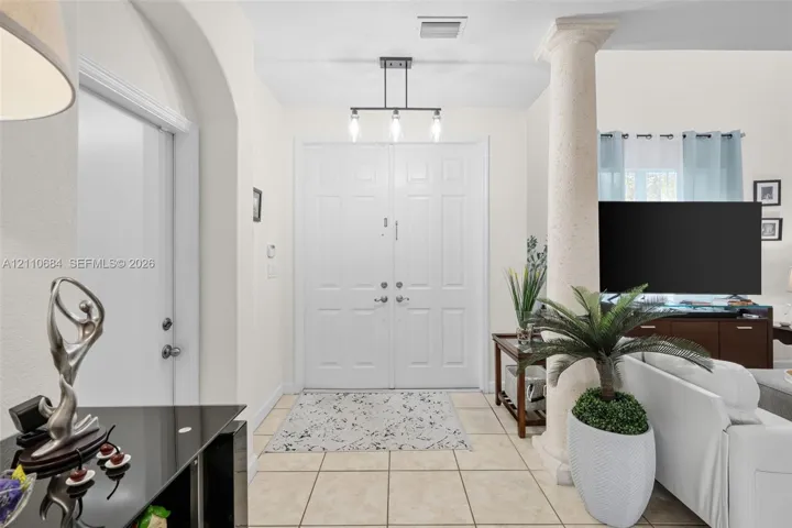 Foyer featuring double entry doors, high ceilings, decorative stone-textured column, and tile flooring