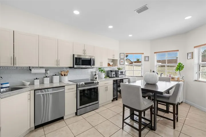 Kitchen featuring light-toned shaker cabinetry, stone-finish countertops, stainless steel appliances, recessed ceiling lighting.