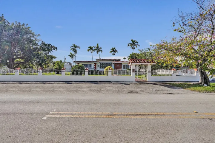 Single-story residence featuring a terracotta-tiled roof, white exterior masonry walls, a decorative metal perimeter fence, and a gated entrance