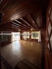 Interior space featuring natural wood-paneled walls, exposed wood-beam ceiling, grid-patterned tile flooring, and multiple windows