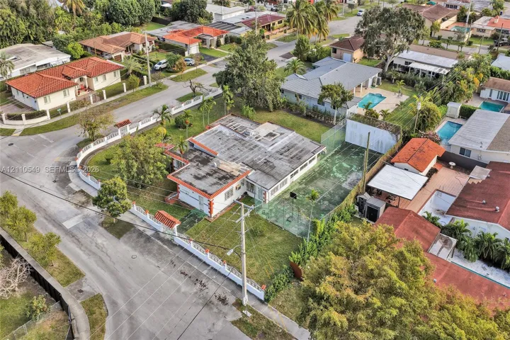 Aerial perspective featuring a corner lot property with a private fenced tennis court and a perimeter masonry wall